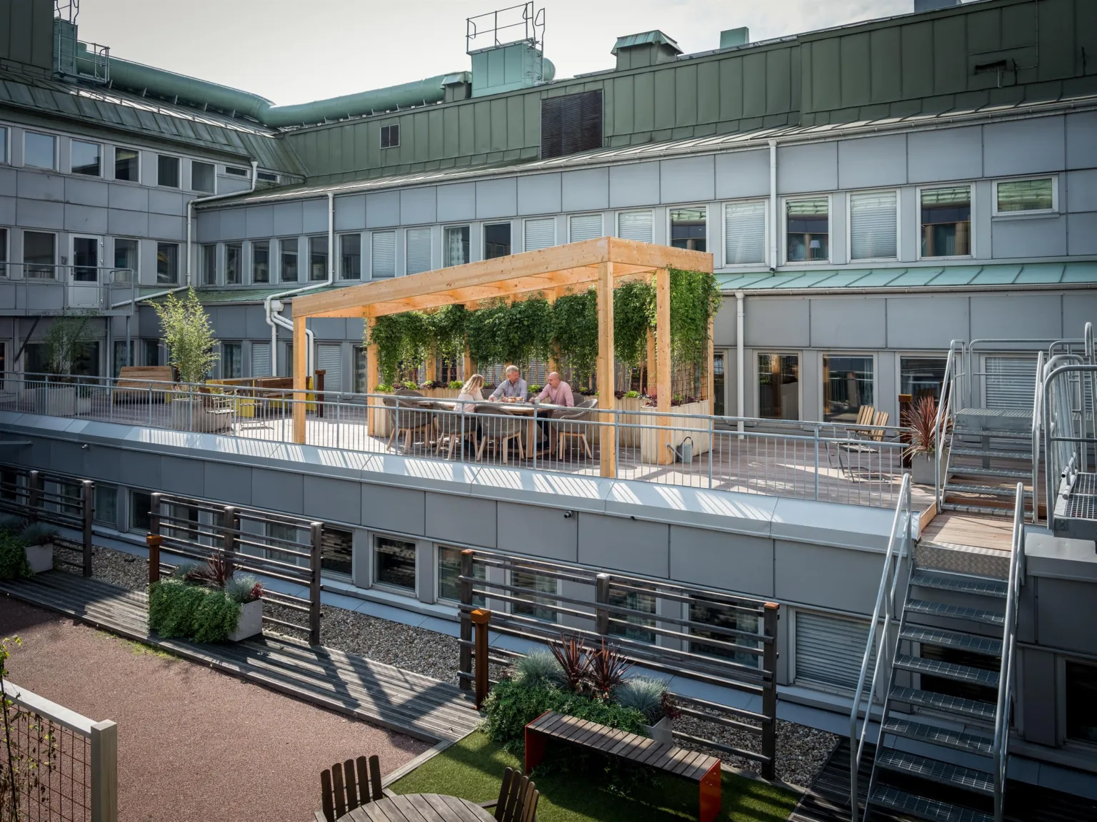 2. En terrass på en byggnad med pergola, grönska och människor som sitter vid bord.