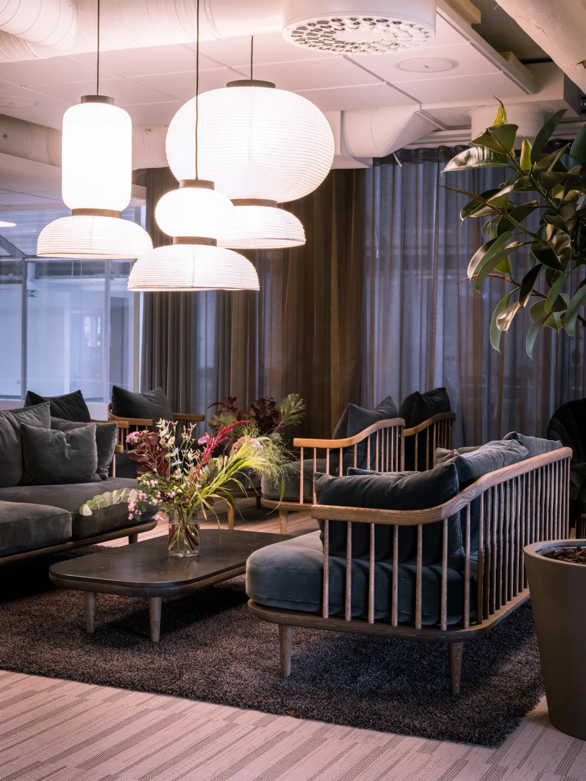3. En elegant lounge med soffor, bord, växter och stora vita taklampor.