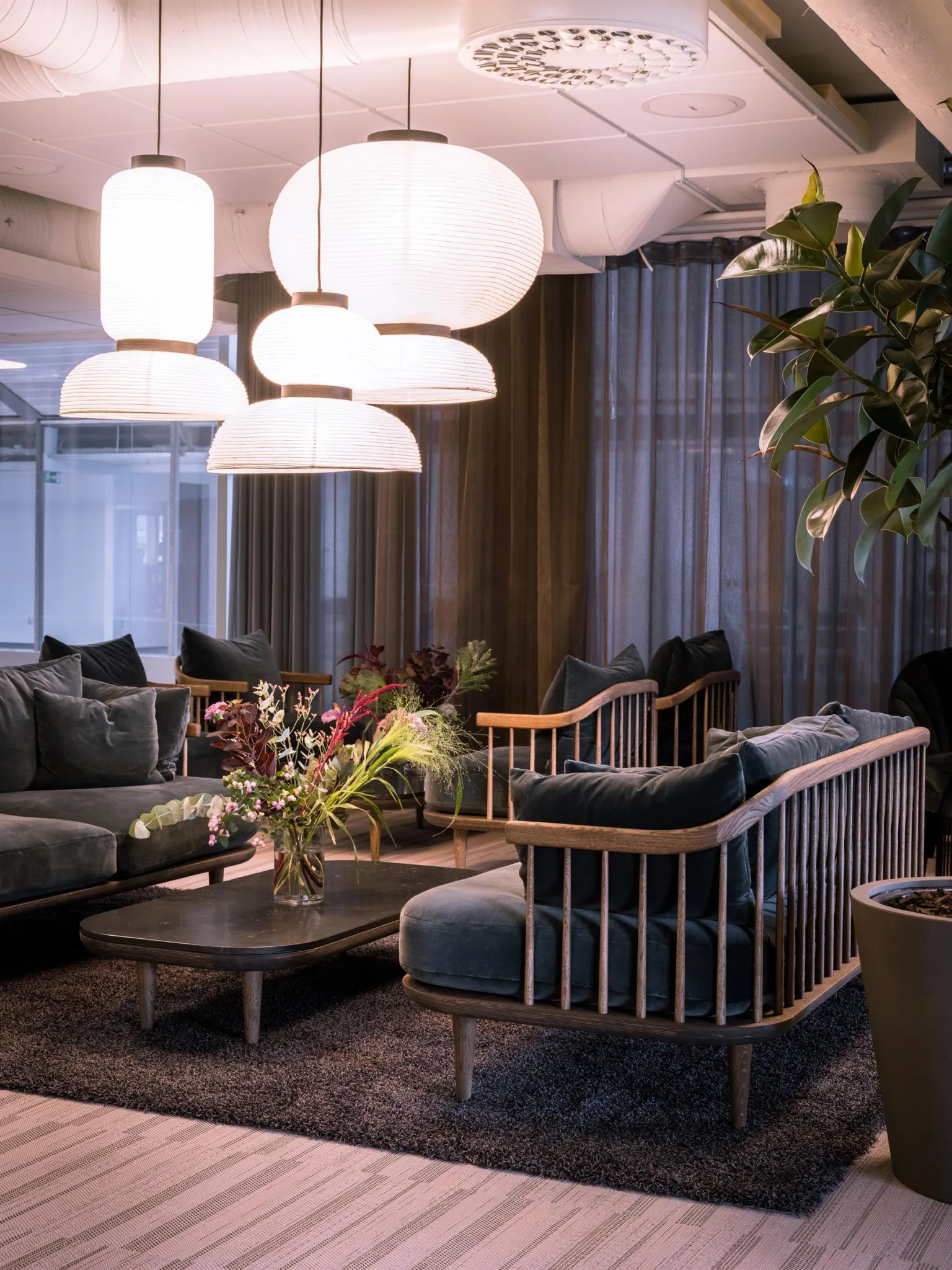 3. En elegant lounge med soffor, bord, växter och stora vita taklampor.