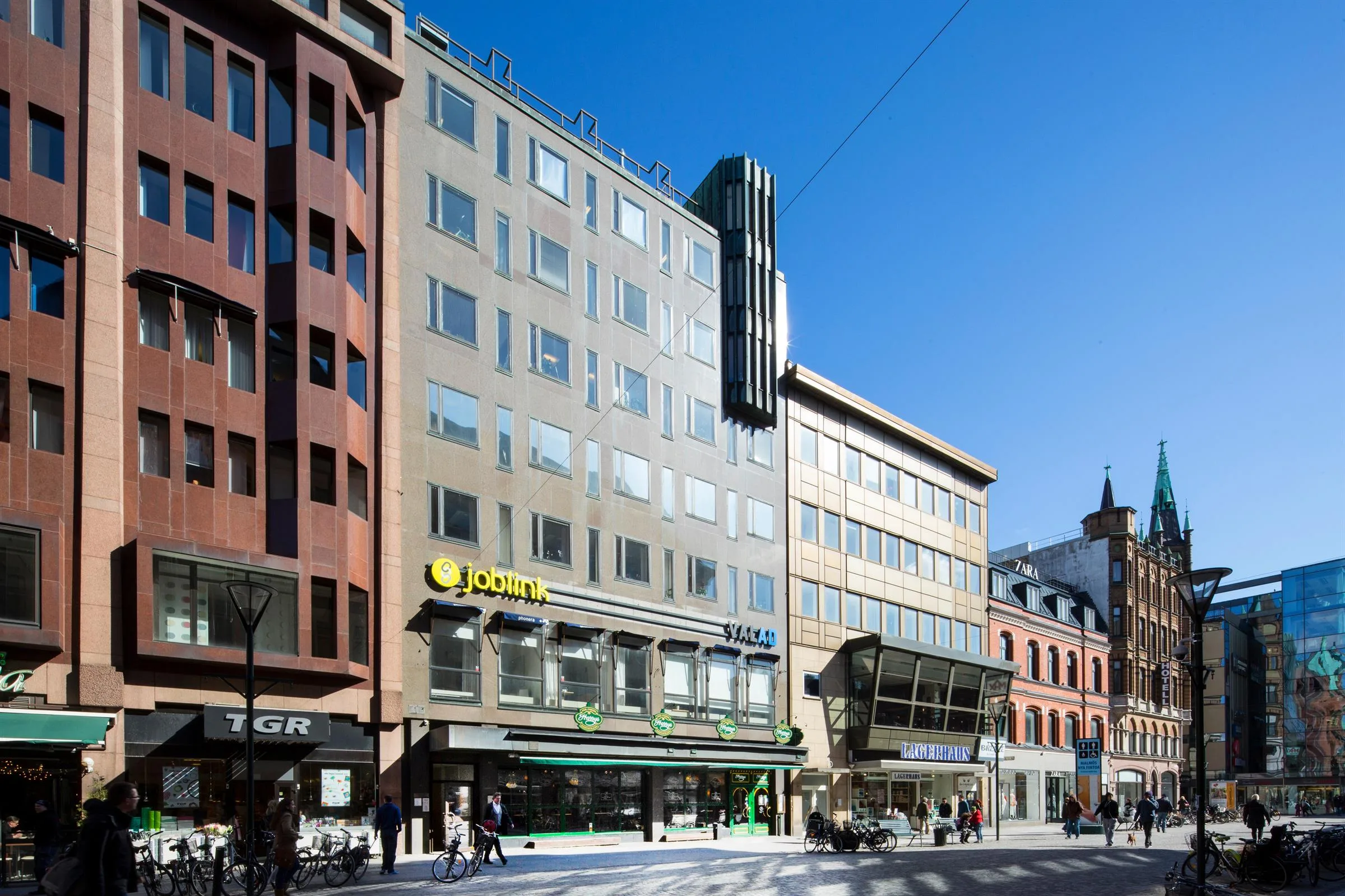1. En modern byggnad med glasfasad, butiksskyltar och blå himmel i stadsmiljö.