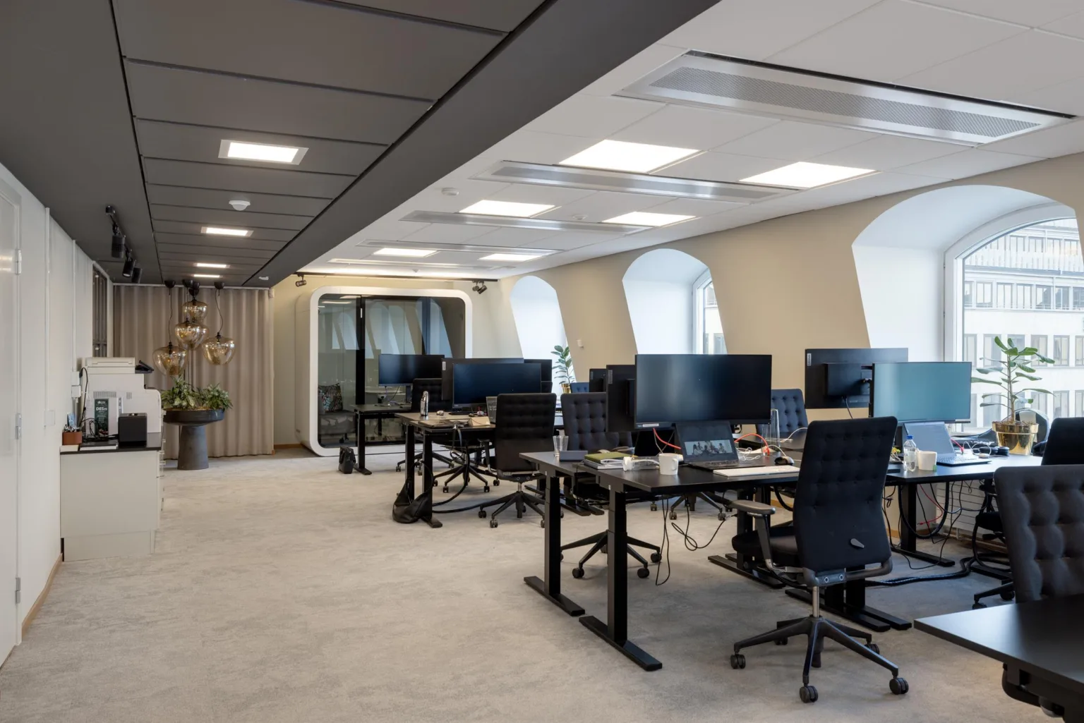 Ett modernt kontor med skrivbord, datorer, kontorsstolar och glasväggar.