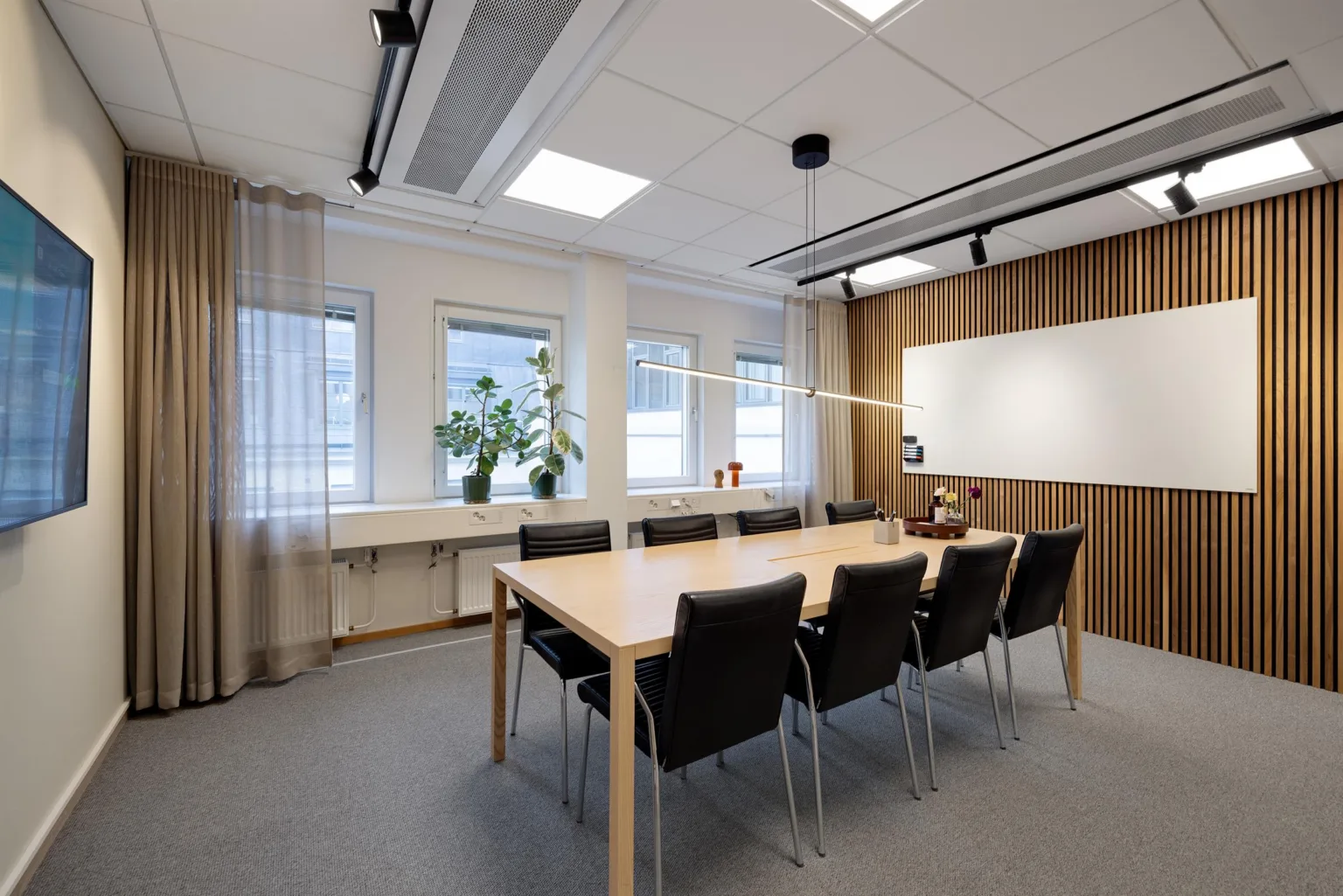 Ett konferensrum med ett bord, flera stolar, tre fönster och en whiteboard på väggen.