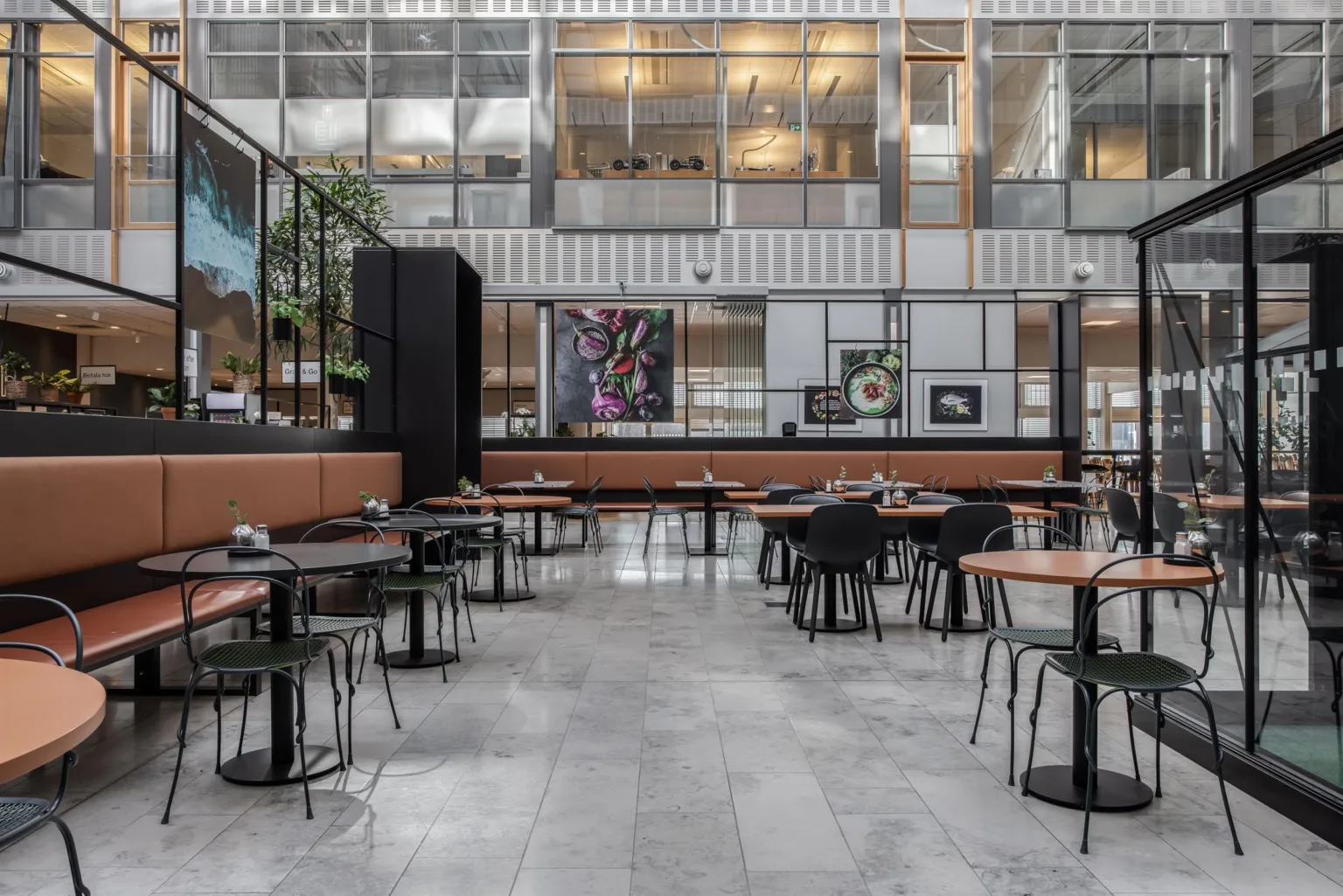 En rymlig restaurang med moderna bord och stolar, samt glasväggar som släpper in naturligt ljus.