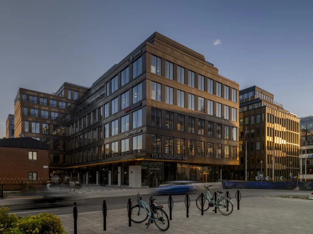 Brun byggnad med glasfönster i skymningsljus, cyklar parkerade vid staket.