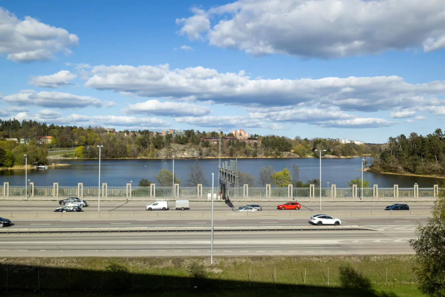 5. En vy över en motorväg, en sjö och träd i bakgrunden under en blå himmel med moln.