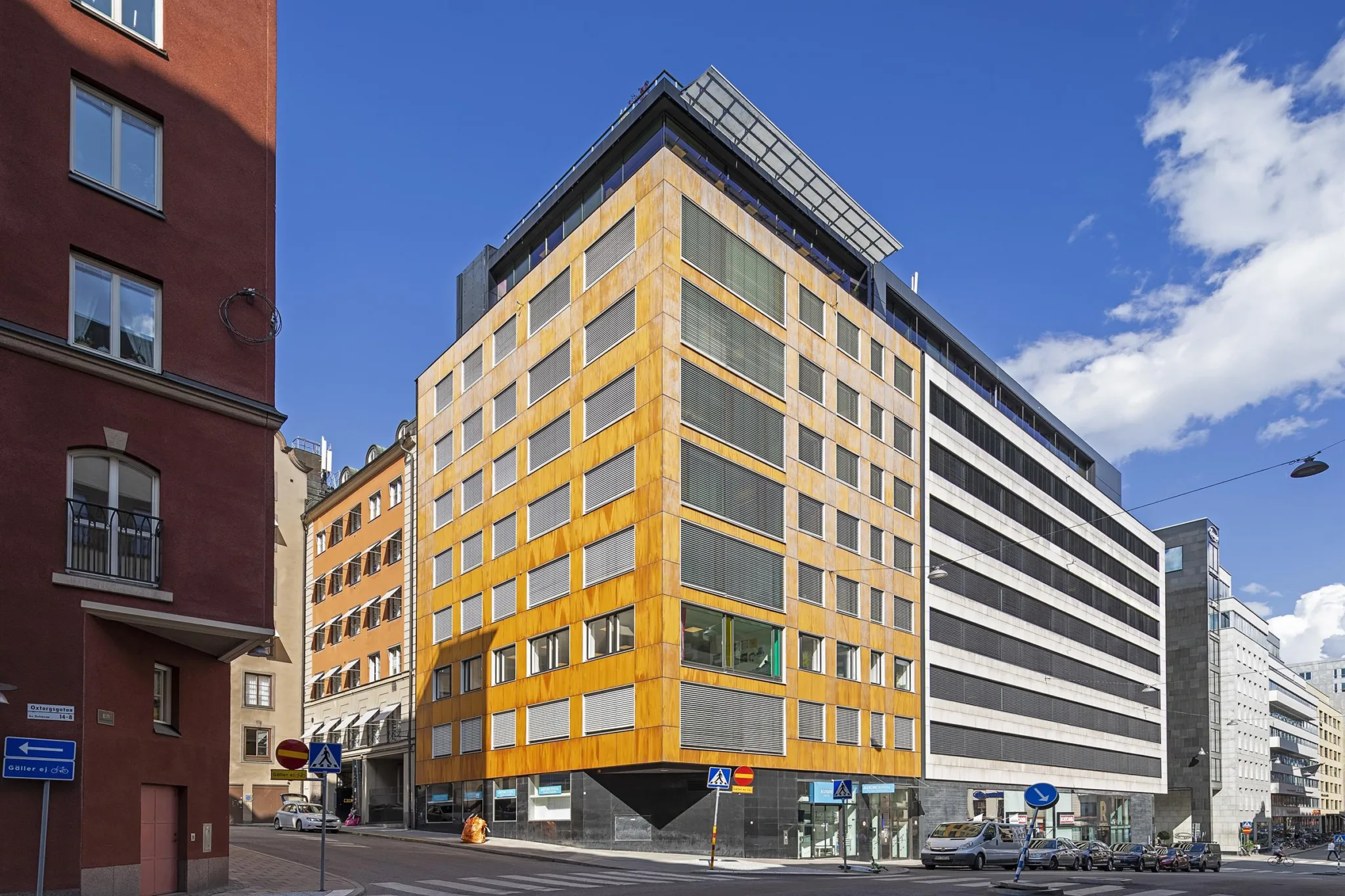 En modern byggnad med gul fasad och stora glasrutor på en stadsgata.