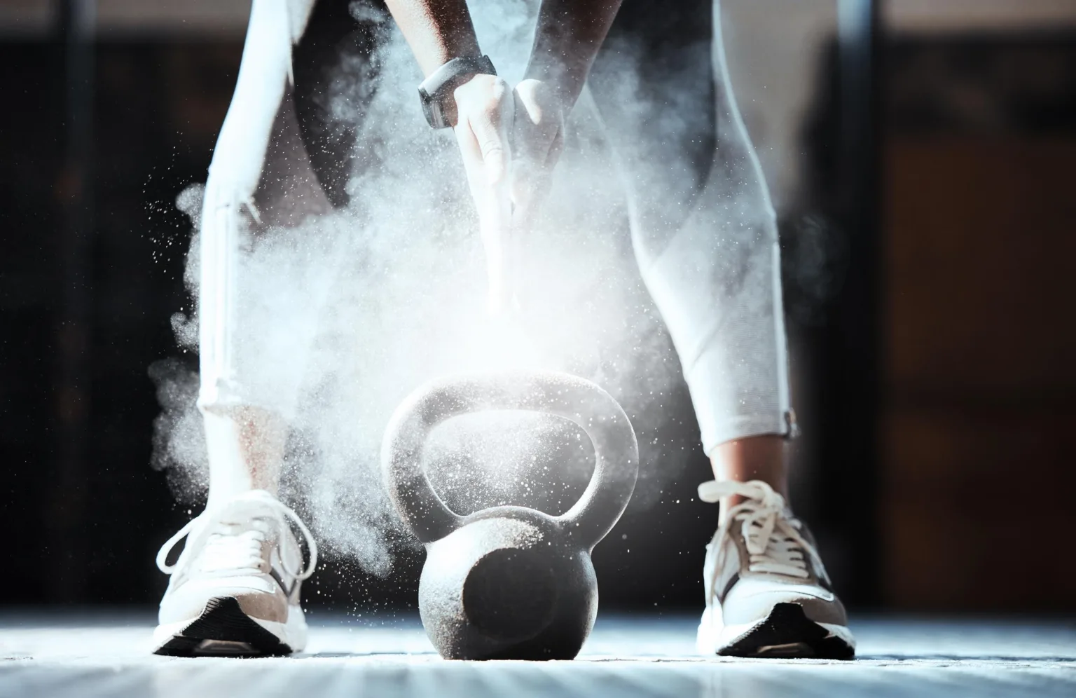 2. En person lyfter en kettlebell, omgiven av damm eller krita, iklädd vita skor och träningskläder.
