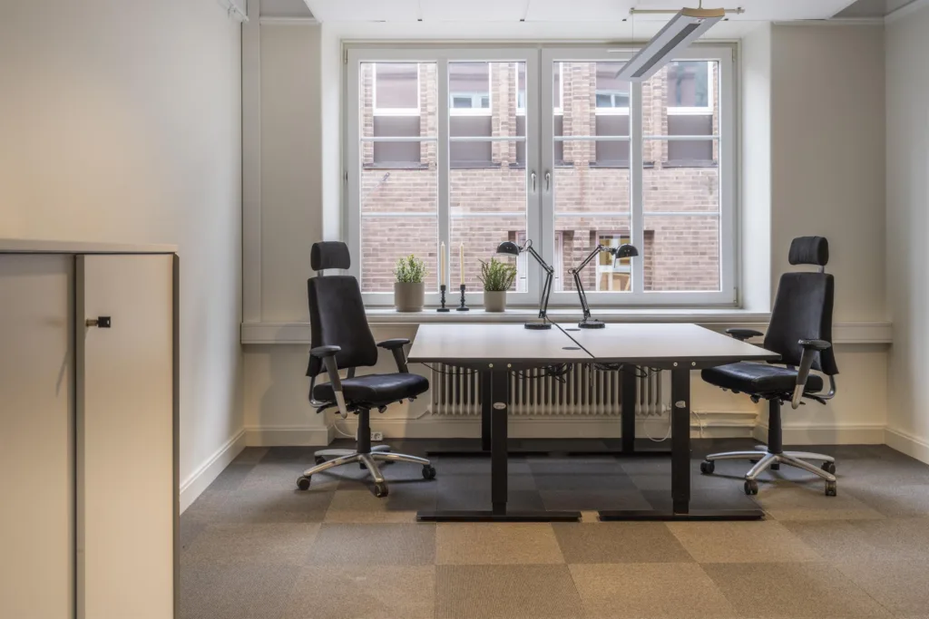 4. Ett kontorsrum med två skrivbord och kontorsstolar framför ett stort fönster.