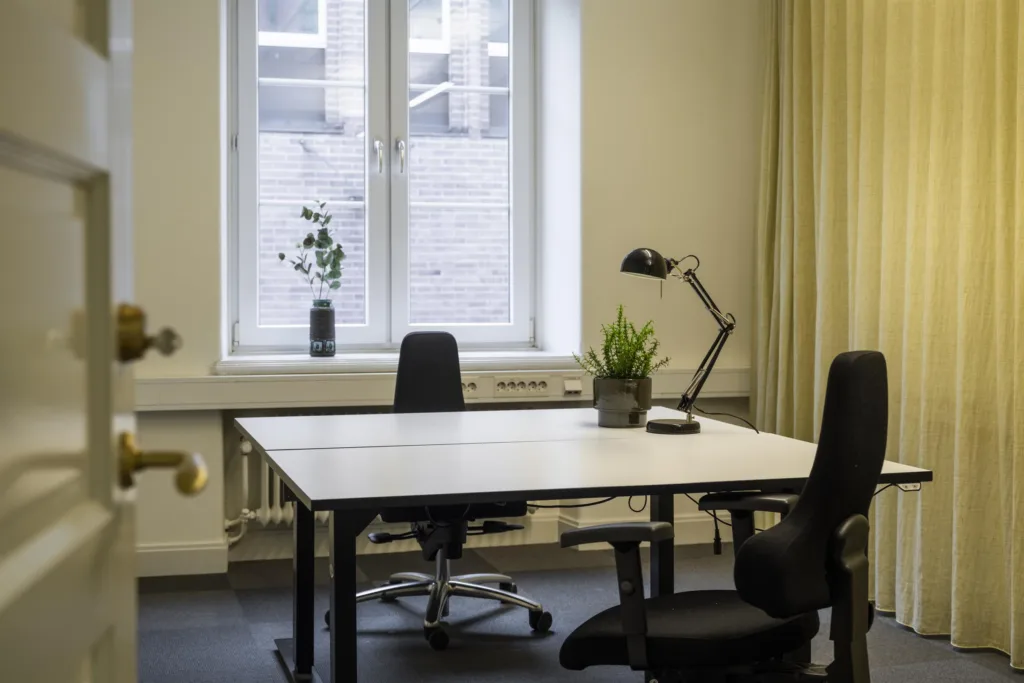 3. Ett kontor med två skrivbordsstolar, ett skrivbord och växter på fönsterbrädan.