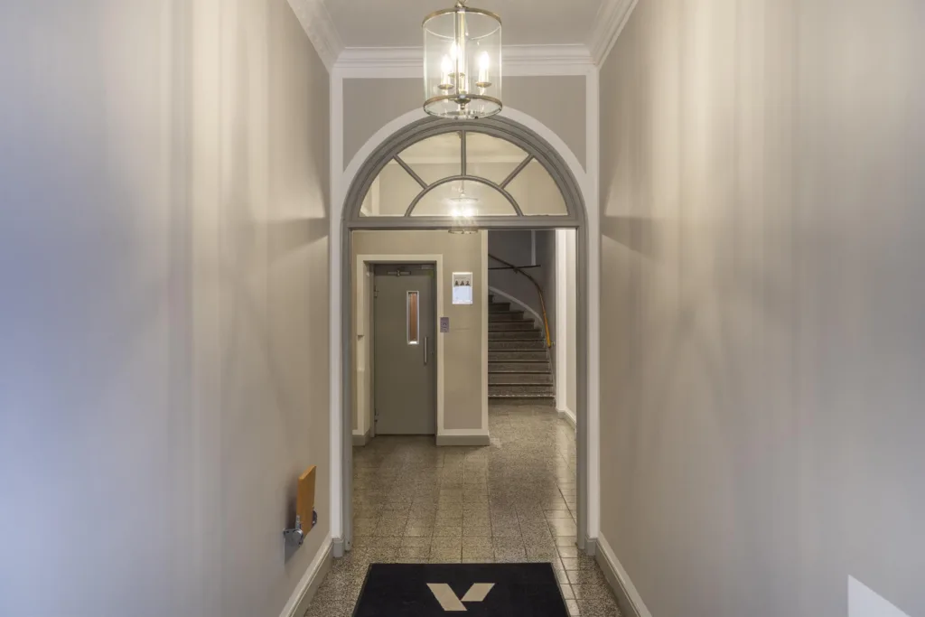 5. En korridor med en valvbåge, en hängande lampa och en dörr i bakgrunden.