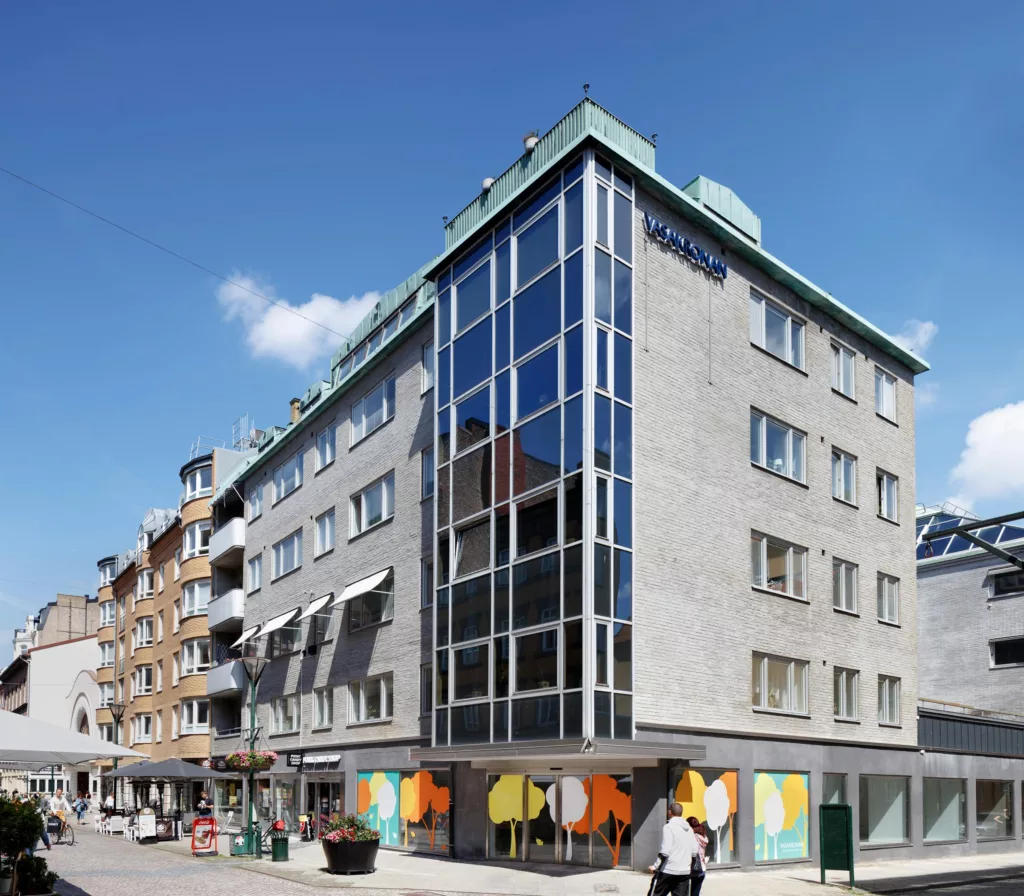 5. Ett hörnhus med stora glasfönster och färgglada dekorationer på bottenvåningen, omgivande byggnader och promenadstråk.
