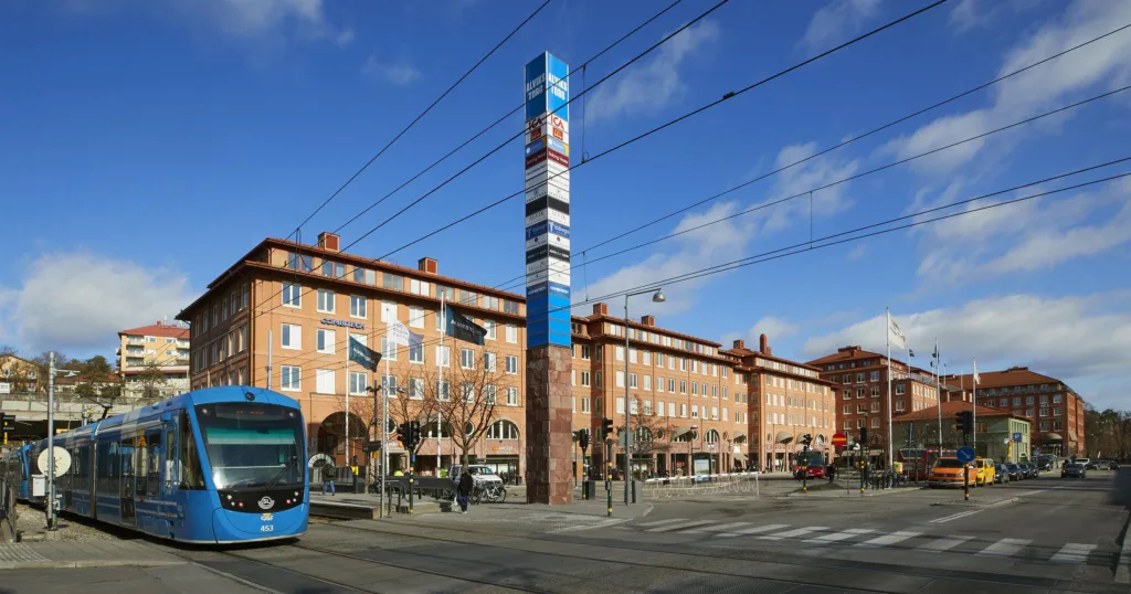 2. En stadsgata med en blå spårvagn och en hög pelare med skyltar framför en tegelbyggnad.