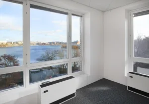 Ett tomt rum med stora fönster som vetter mot en sjö och landskap utanför.