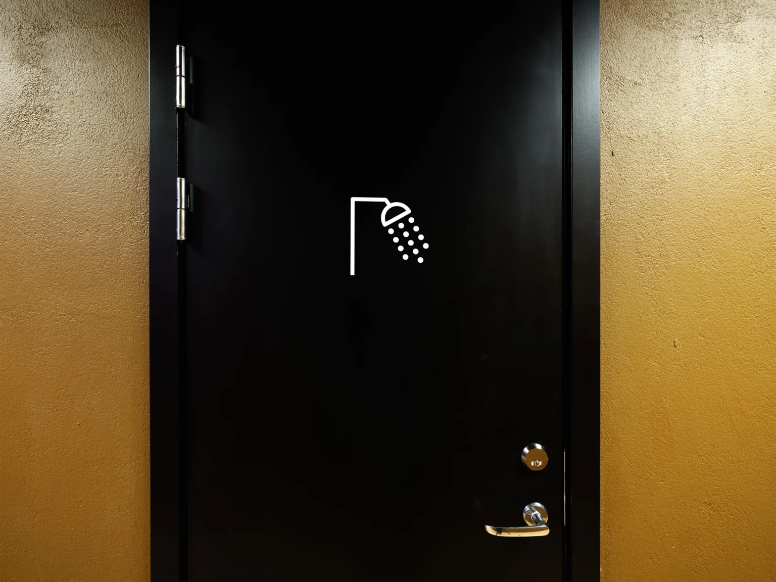 5. Svart dörr med en symbol av en dusch på, omgiven av orangefärgade väggar.