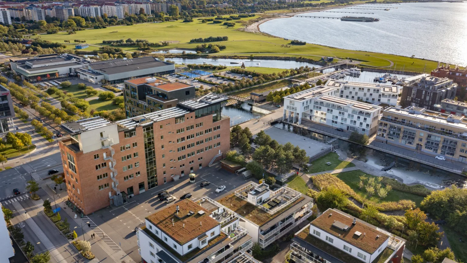 4. Flygfoto över ett bostadsområde nära en kust, med gröna områden och moderna byggnader.