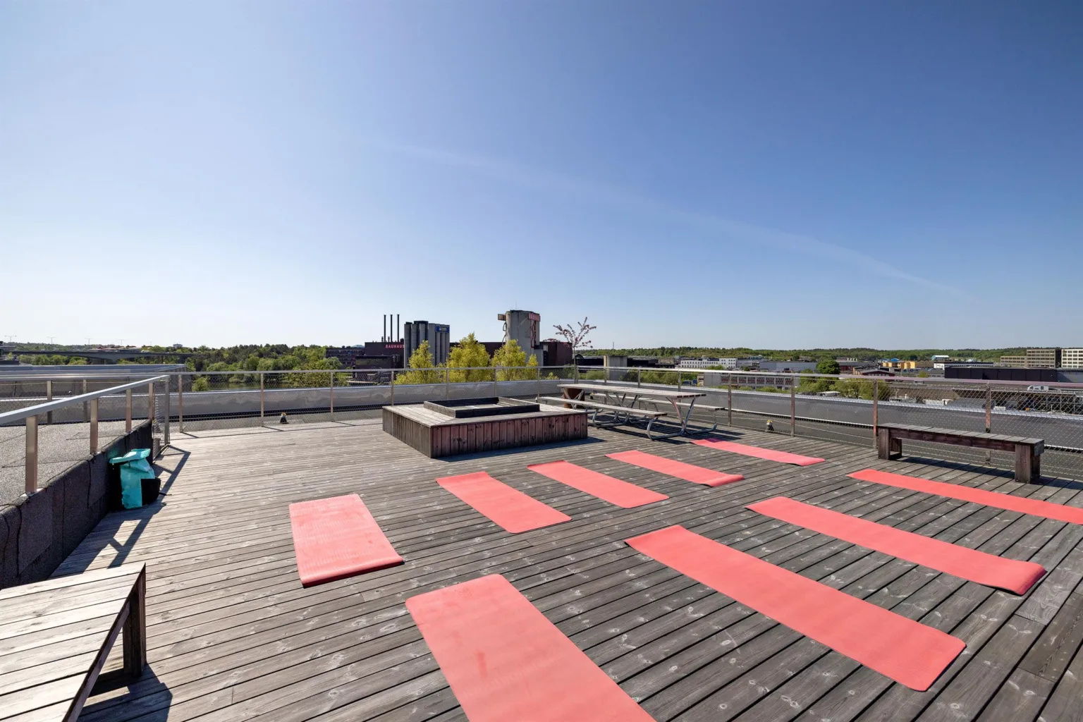 En takterrass med röda yogamattor placerade på ett trädäck och utsikt över omgivande byggnader.