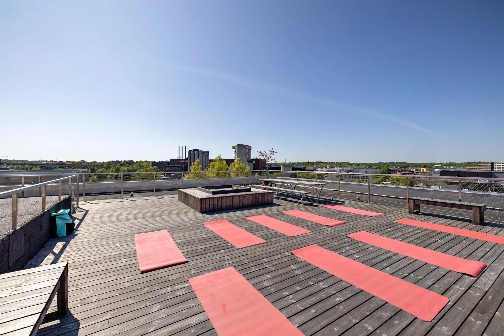 En takterrass med röda yogamattor placerade på ett trädäck och utsikt över omgivande byggnader.