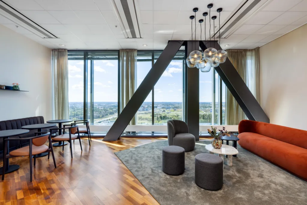 5. Loungeområde med moderna möbler, en röd soffa, små bord och stora fönster med utsikt över landskapet.
