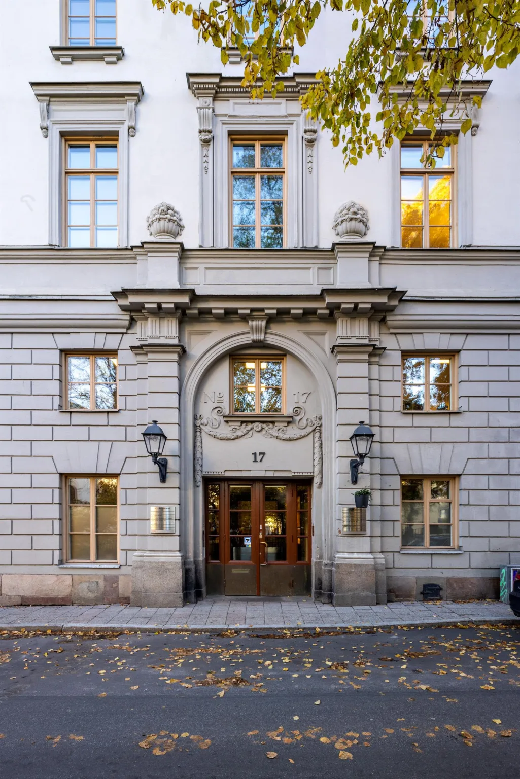 En historisk byggnadsentré med stenfasad, dekorationer och två lampor vid dörren.