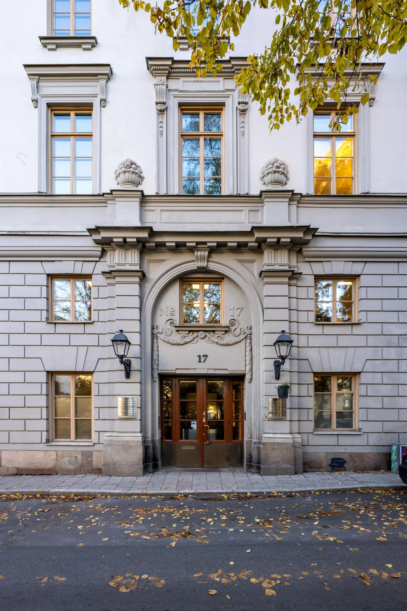 En historisk byggnadsentré med stenfasad, dekorationer och två lampor vid dörren.