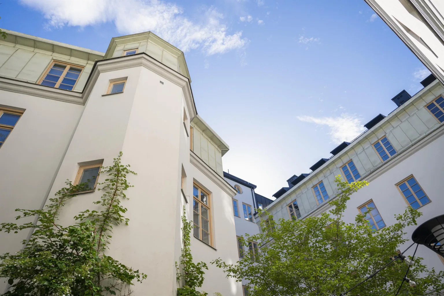 En vit byggnad med tornliknande arkitektur och gröna växter mot en klar blå himmel.