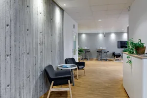 Loungeområde med svarta stolar, små bord och betongväggar.