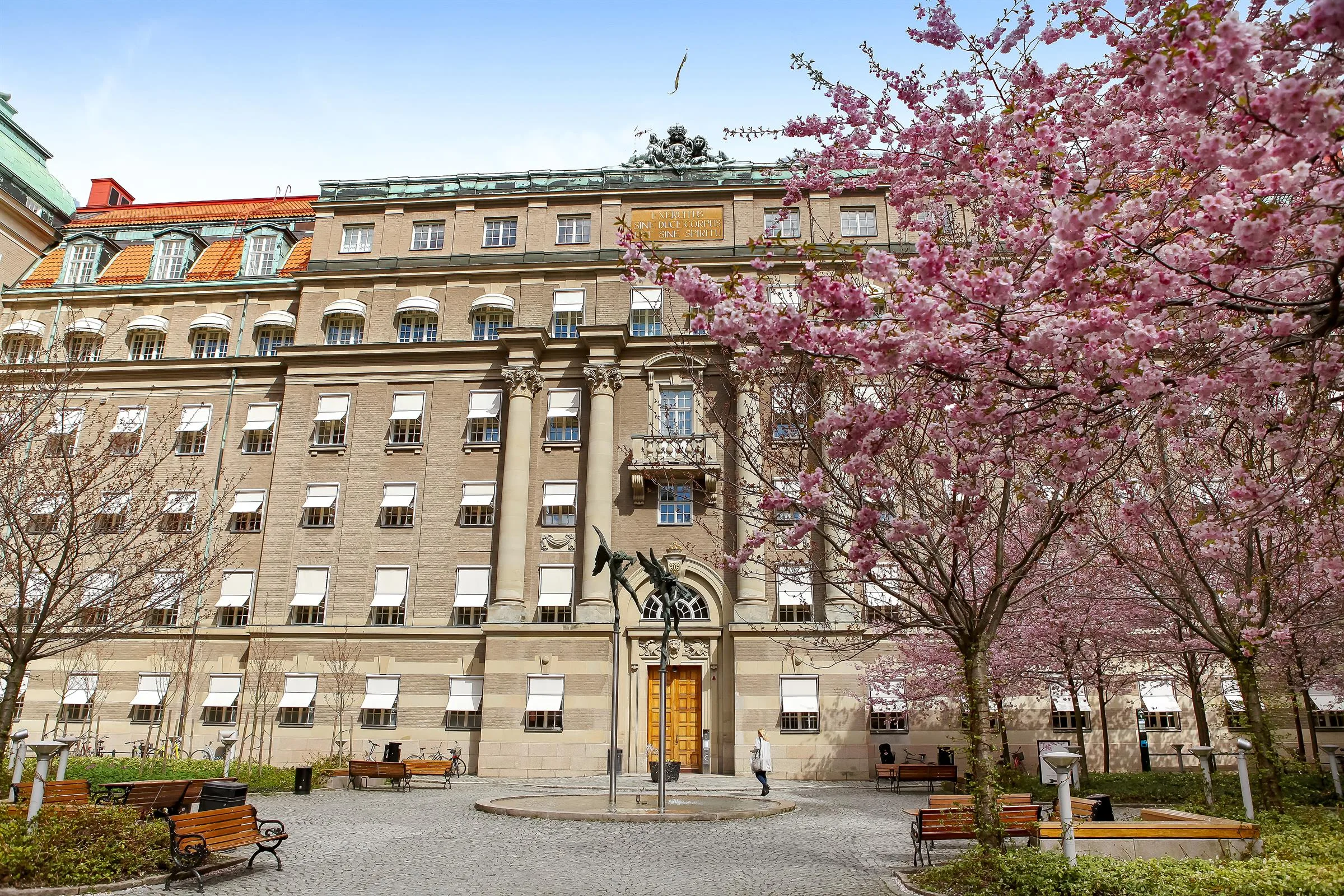 En stor byggnad med körsbärsträd i blom vid en innergård och en gyllene dörr i mitten.