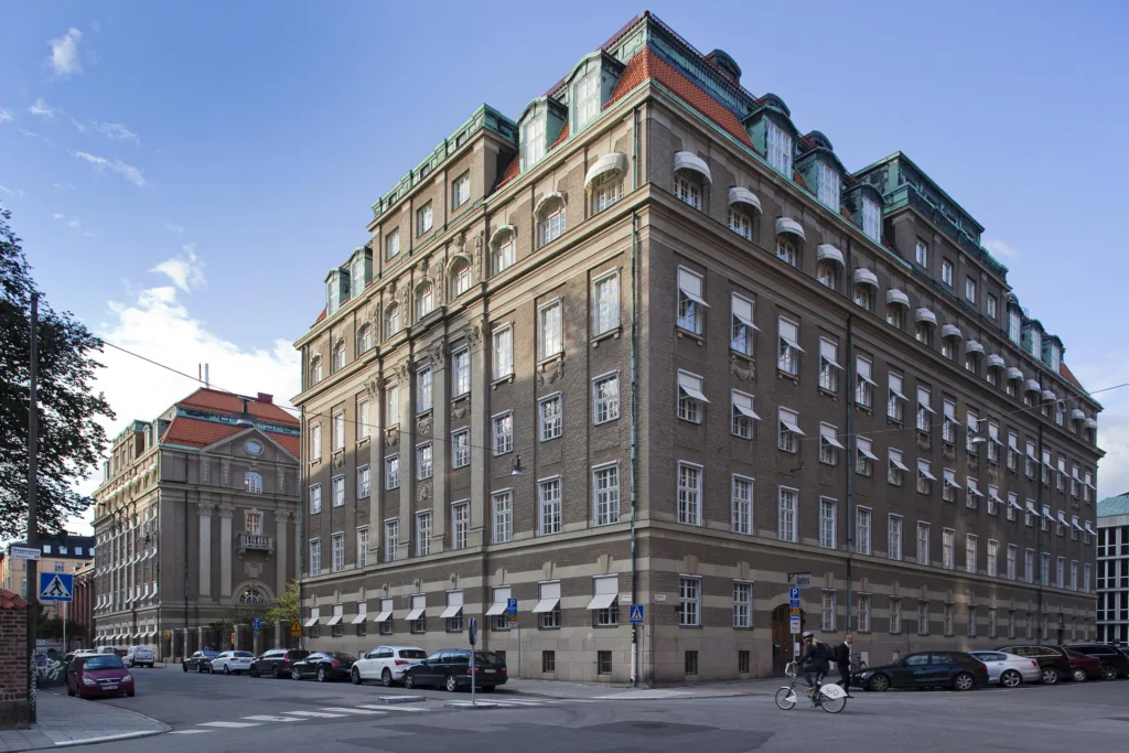 1. En klassisk byggnad med flera våningar, stora fönster och ett hörnläge, omgiven av stadsmiljö.