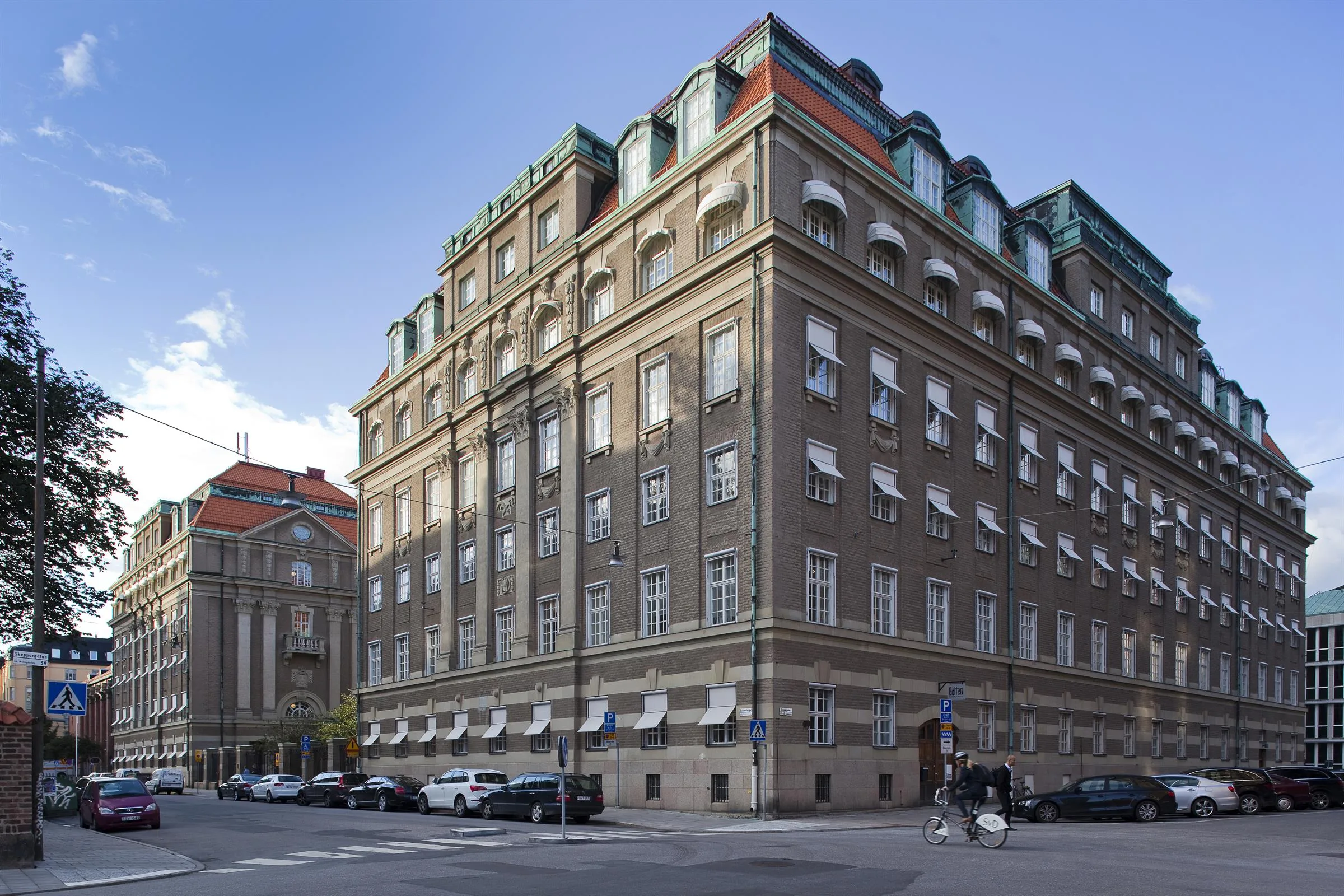 1. En klassisk byggnad med flera våningar, stora fönster och ett hörnläge, omgiven av stadsmiljö.