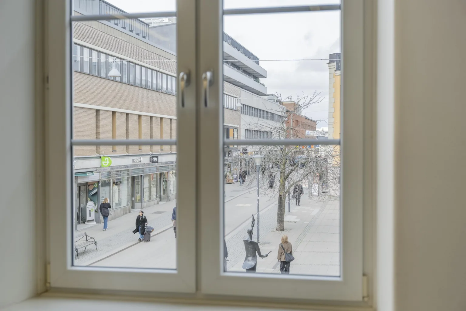 2. Utsikt genom ett fönster som visar en stadsgata med människor som promenerar och byggnader i bakgrunden.