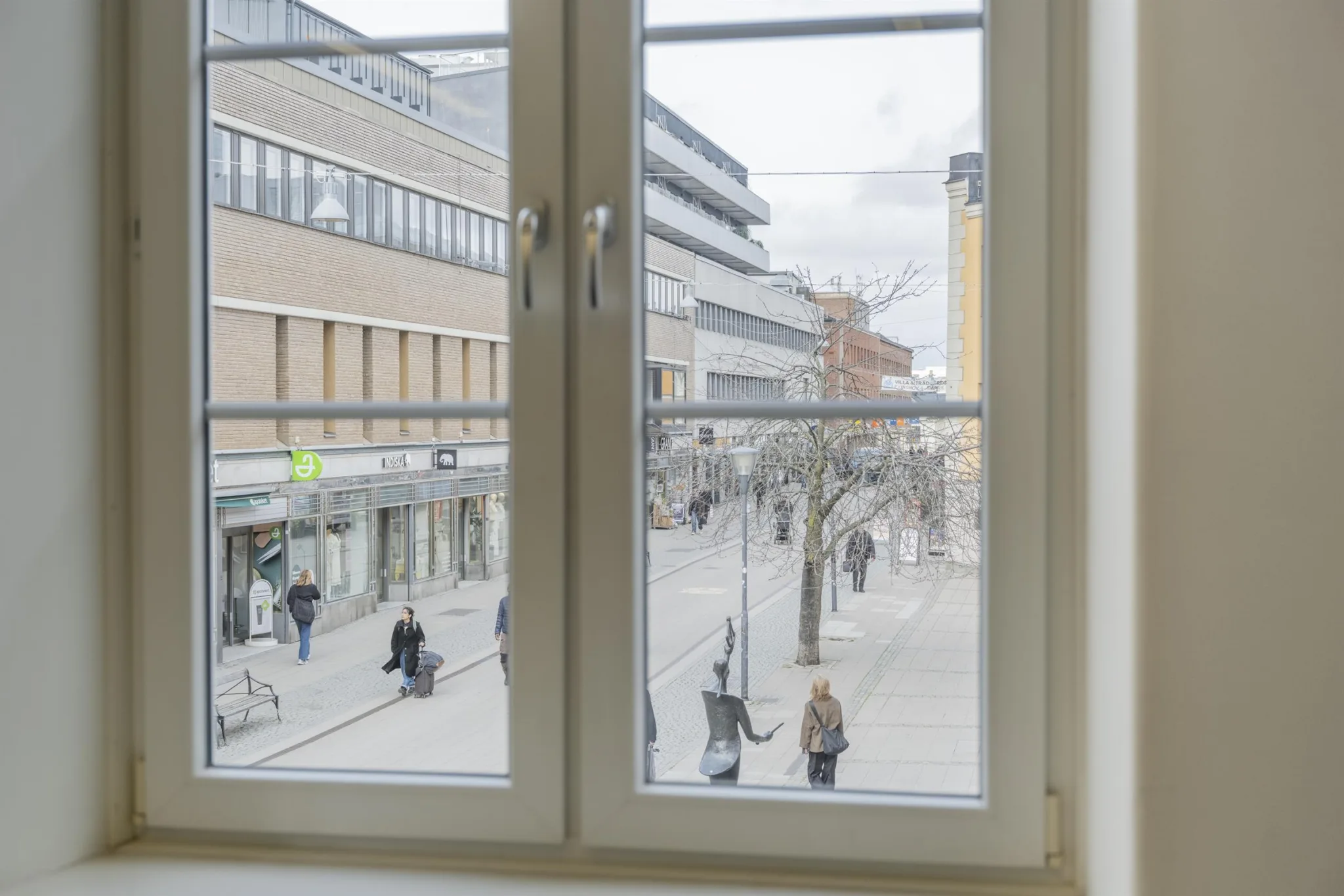 2. Utsikt genom ett fönster som visar en stadsgata med människor som promenerar och byggnader i bakgrunden.