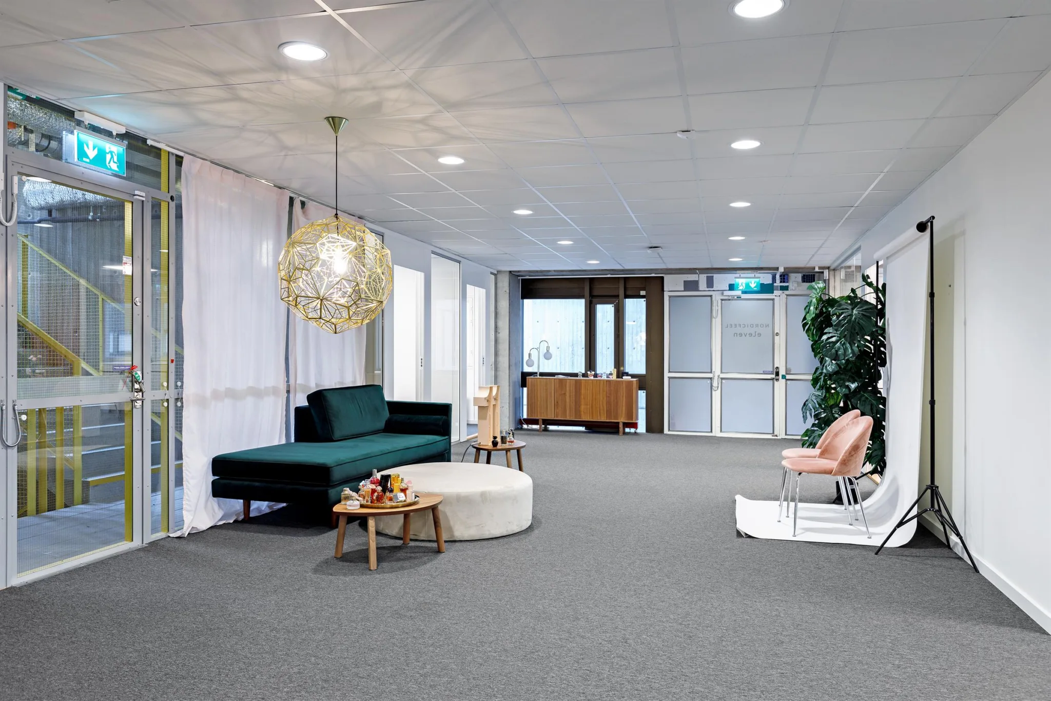 Ett modernt väntrum med en grön soffa, runda bord och en dekorativ hängande lampa.