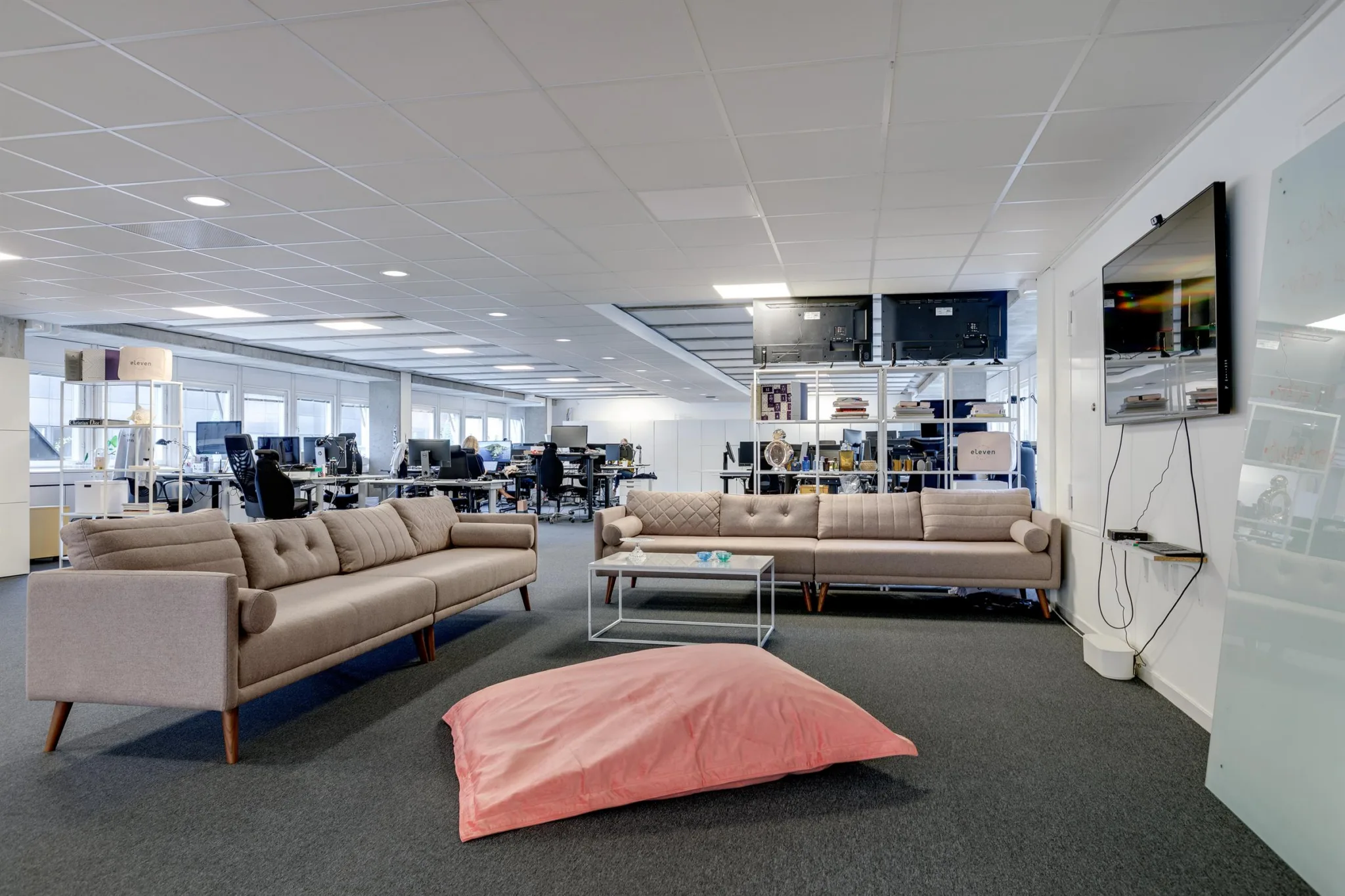 3. Loungeområde med beige soffor, ett soffbord och en rosa sittkudde på en grå matta.