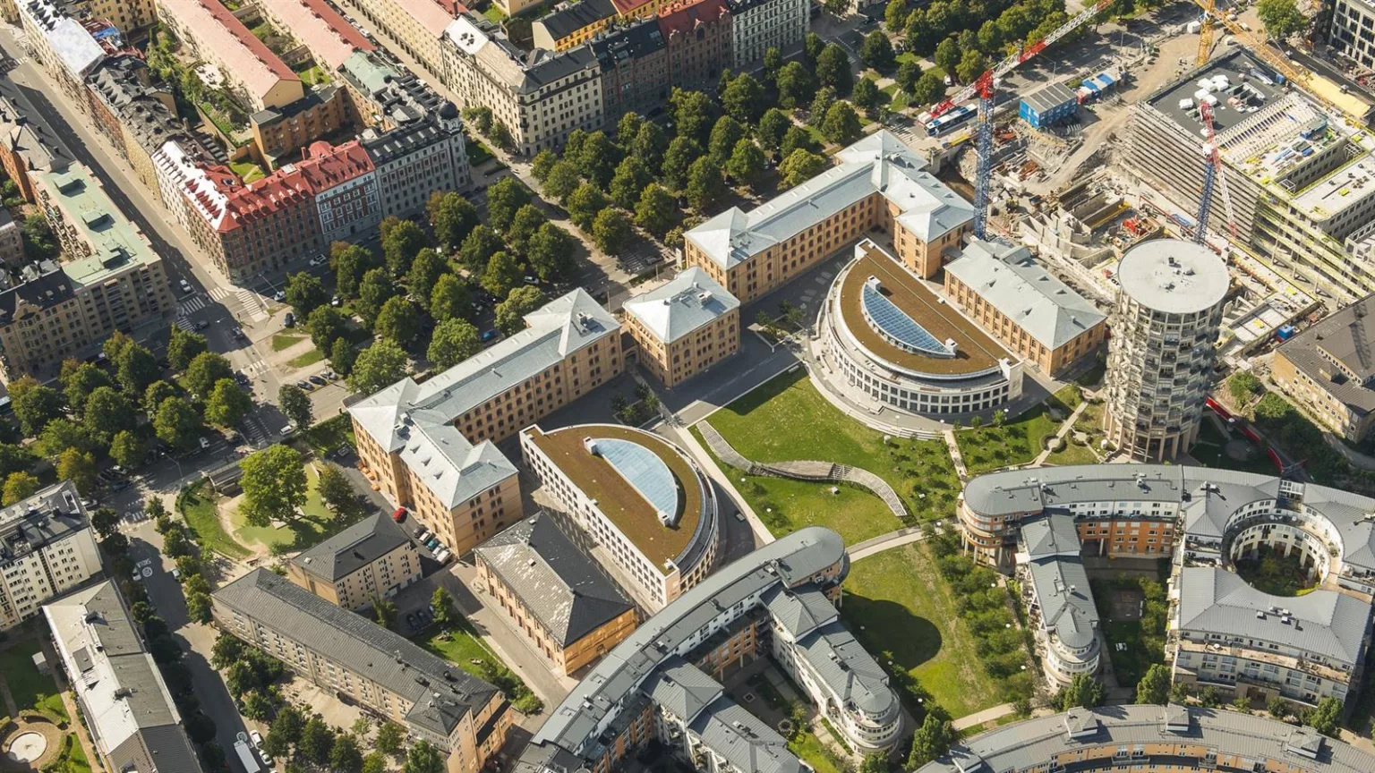 Flygfoto över ett område med symmetriska byggnader, grönska och gångvägar.