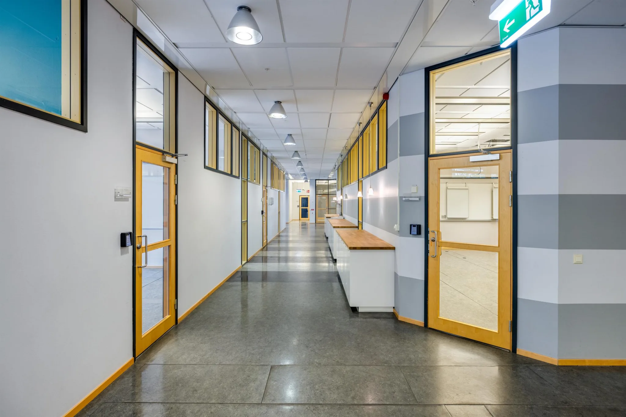 En lång korridor med glasdörrar och vita skåp längs ena sidan.