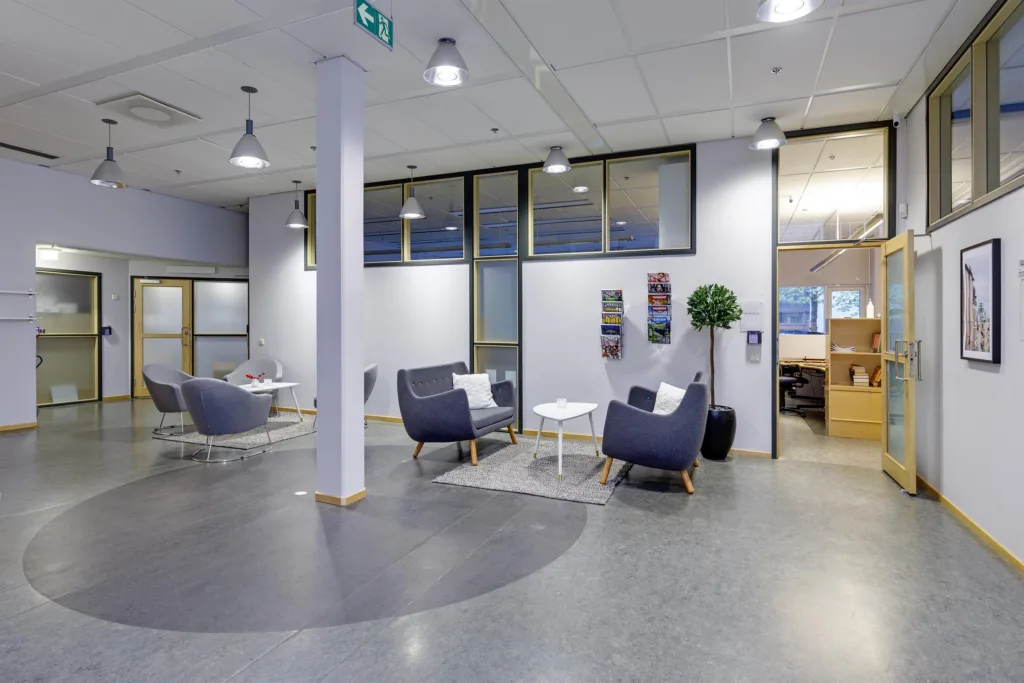 5. Ett mötesområde med fåtöljer, små bord och väggdekorationer, beläget i ett modernt kontorsutrymme.