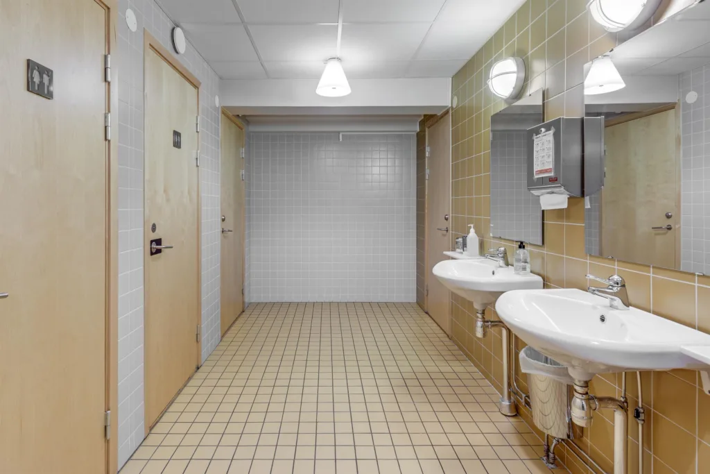 1. Ett badrum med två handfat, speglar och beige kakelväggar.