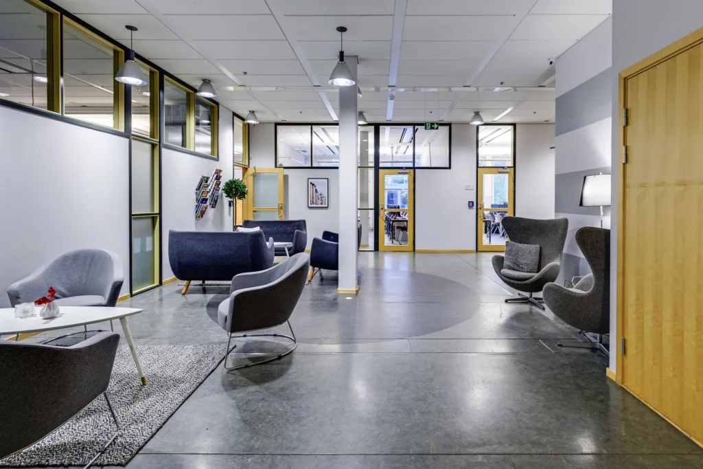 En modern lounge med fåtöljer, soffor och glasväggar som delar utrymmet.