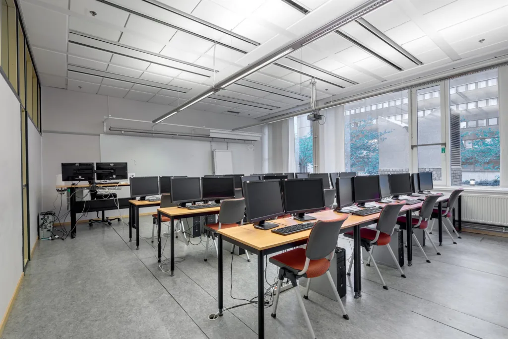 Ett datorrum med flera arbetsstationer, stolar och stora fönster som släpper in ljus.