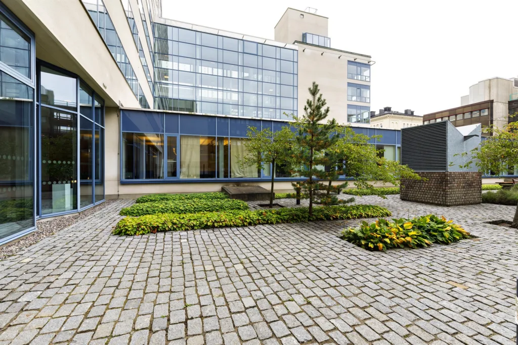 5. En stenlagd innergård med grönska, träd och en modern byggnad omgiven av glasväggar.