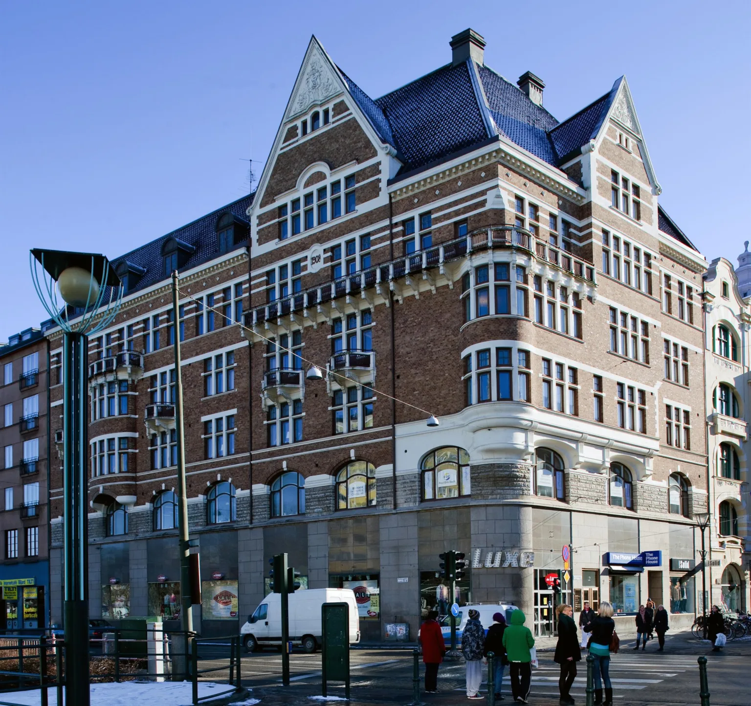 4. En stor tegelbyggnad med spetsigt tak och många fönster, omgiven av gatulampor och människor på gatan.