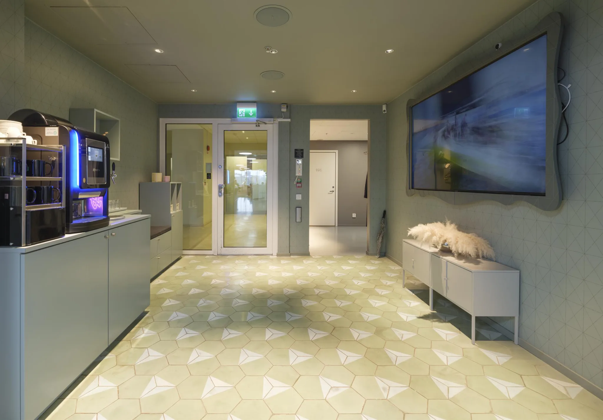 1. En modern entré med ljusgul golvdesign, sittplatser och en stor väggmonterad skärm.