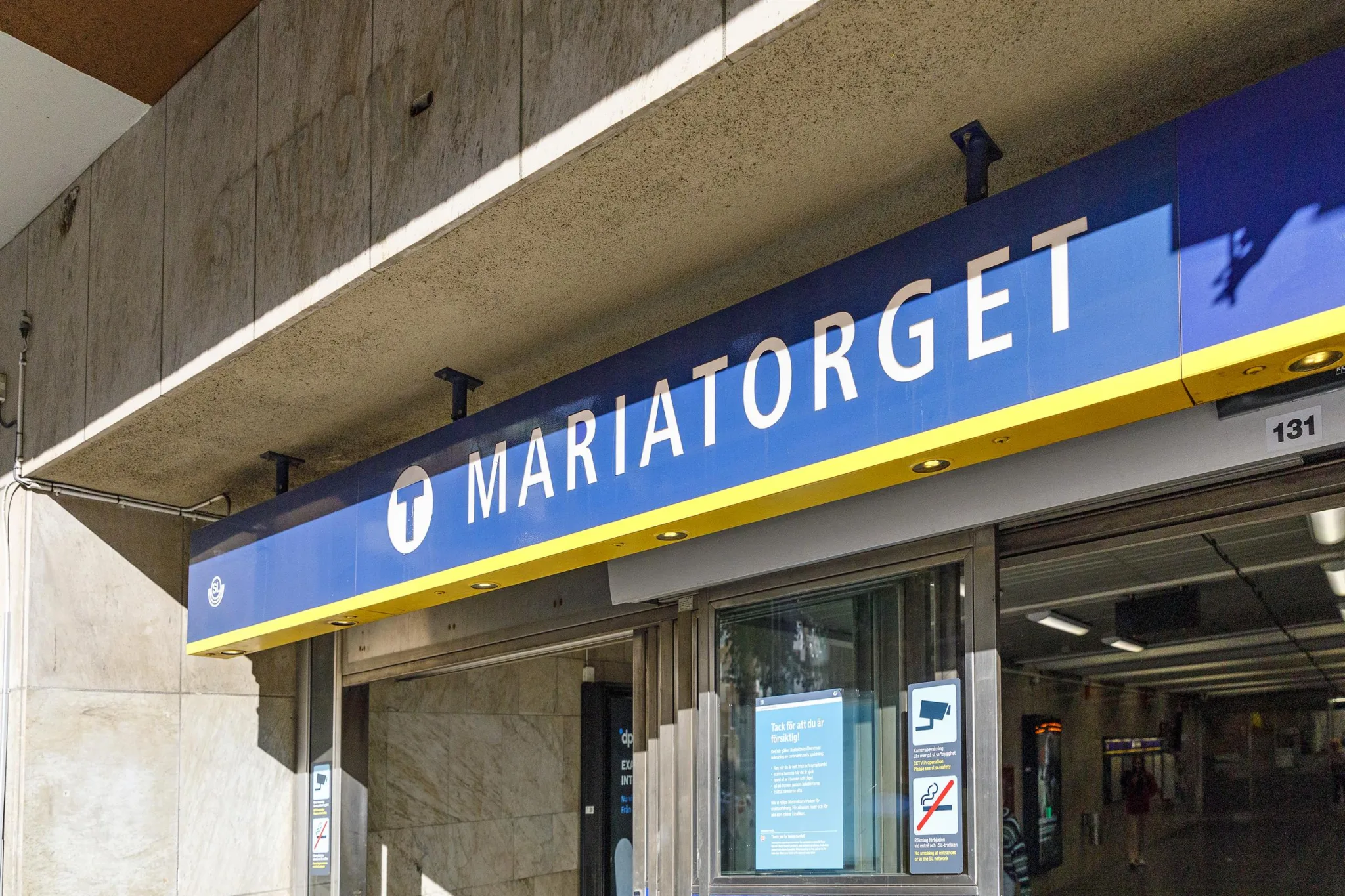 En blå skylt med texten "Mariatorget" ovanför en ingång till en tunnelbanestation.