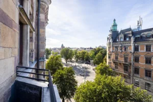 5. Utsikt från en balkong över ett torg med träd samt stora historiska byggnader.