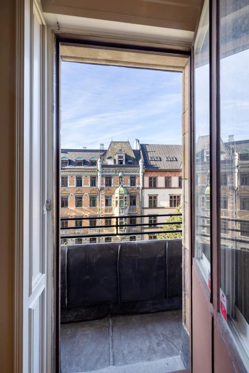 3. En öppen balkongdörr med utsikt över stadens byggnader och blå himmel.