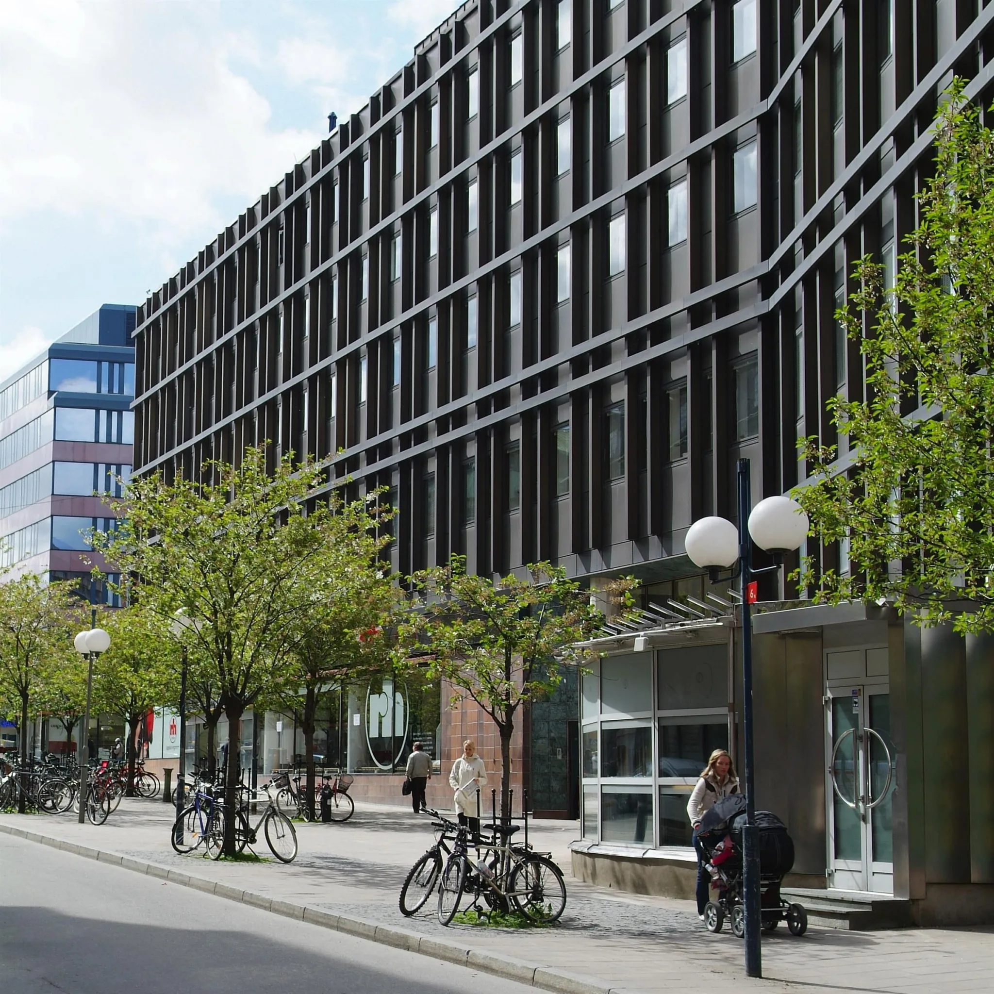 5. En stadsgata med moderna byggnader, träd och cyklar parkerade längs trottoaren.