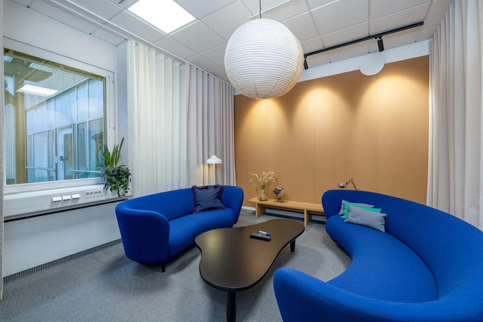 Ett väntrum med två blå soffor, ett svart soffbord, en stor vit taklampa och en beige vägg.