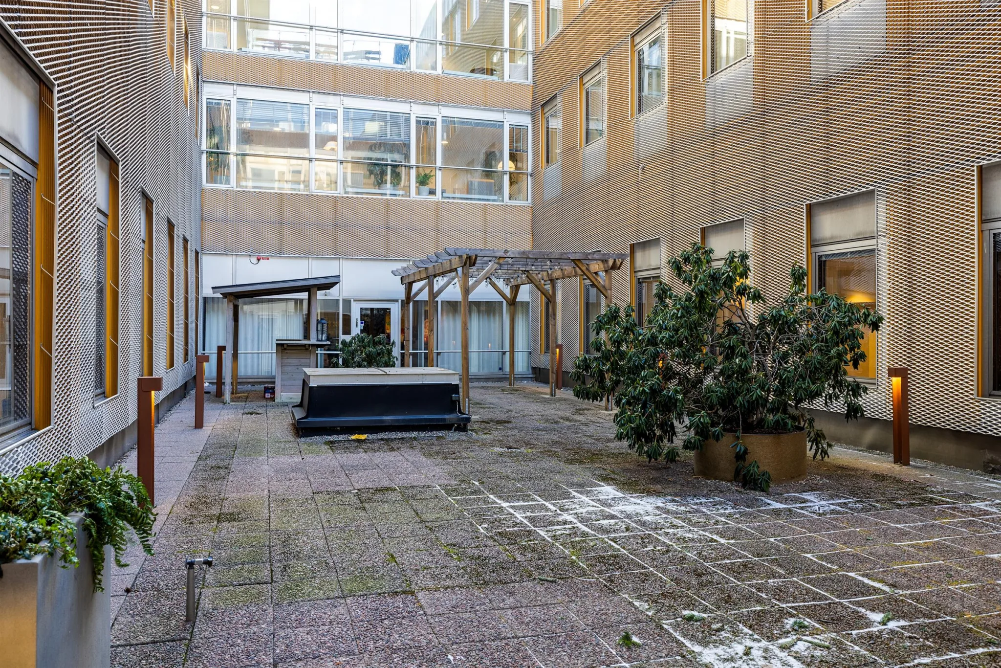 En innergård med stenläggning, trädgårdsdekorationer och byggnader med stora fönster runtom.