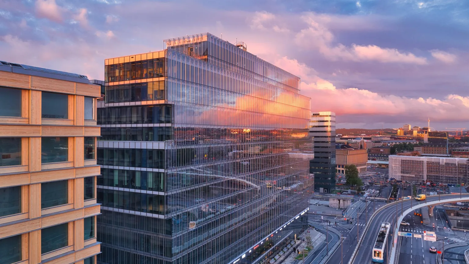 1. En modern glasbyggnad reflekterar en färgstark solnedgång, med omgivande stadsmiljö och vägar.