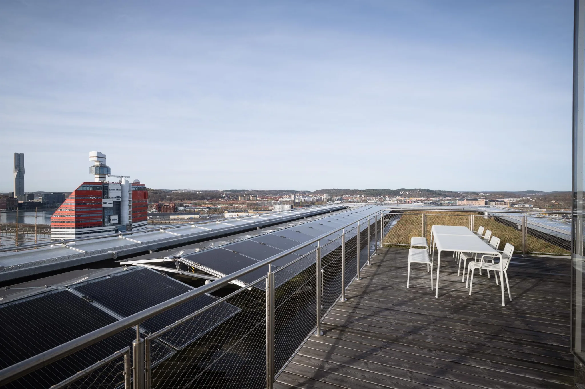 En takterrass med solpaneler, bord och stolar, med utsikt över stadens byggnader och landskap.